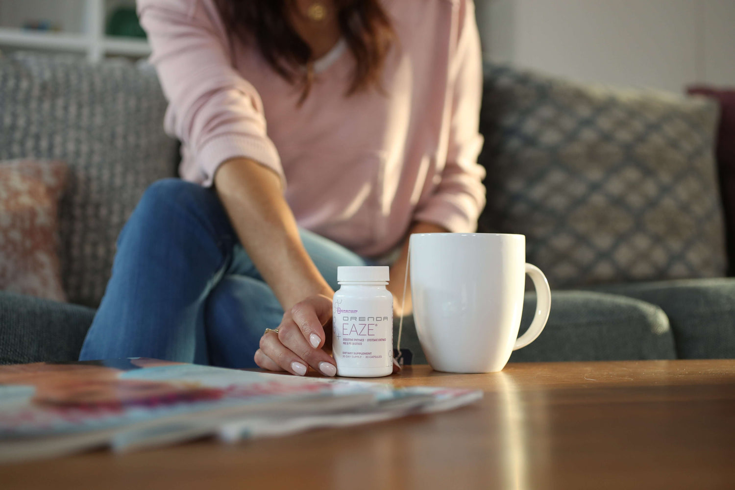 Woman reaching for a bottle of Orenda Eaze on a coffee table next to a cup of tea