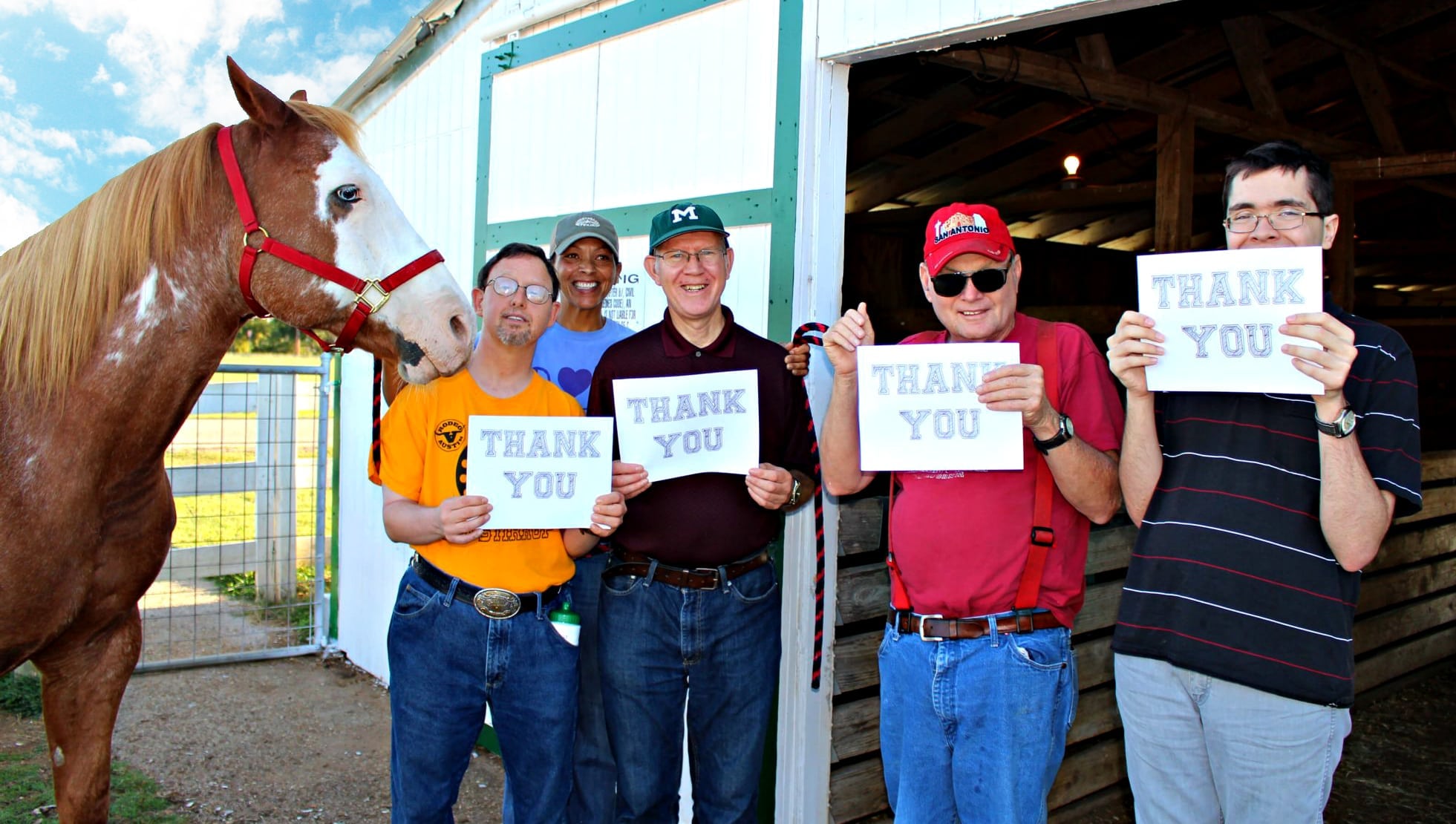 Group of Marbridge Charity members holding up thank you signs by a horse in door of barn
