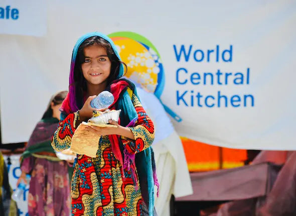 World Central Kitchen Charity photo of a girl in colorful clothes holding food and water bottle